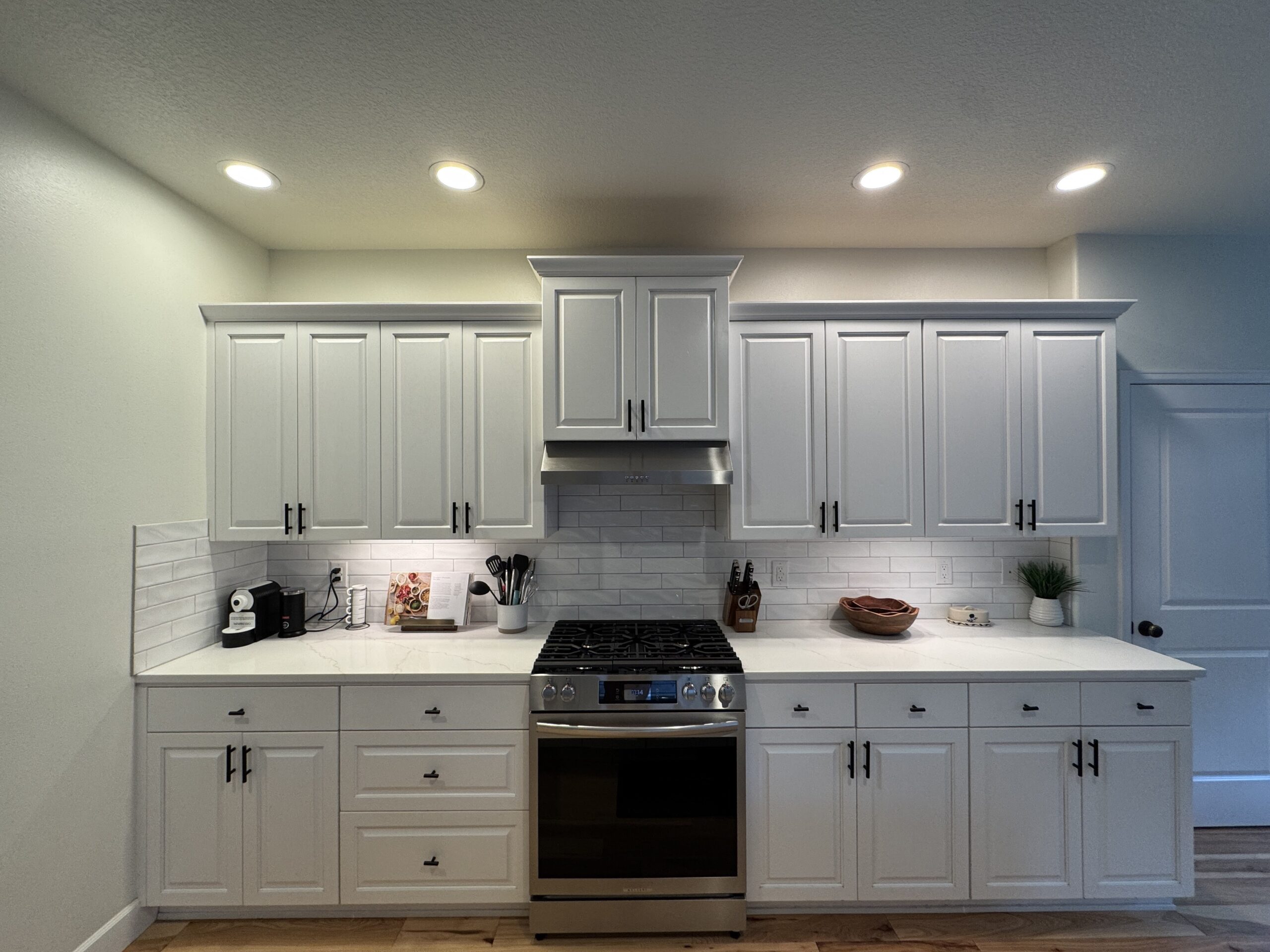 White kitchen cabinetry with black hardware, light countertops, and a tiled backsplash
